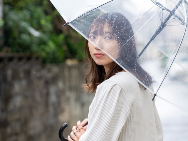 雨が降る日に傘をもった女性が不安そうに立っている様子