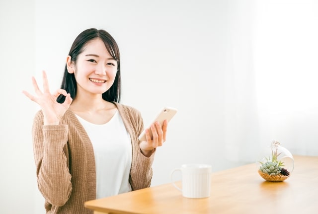 スマートフォンを持ちokサインをしている女性